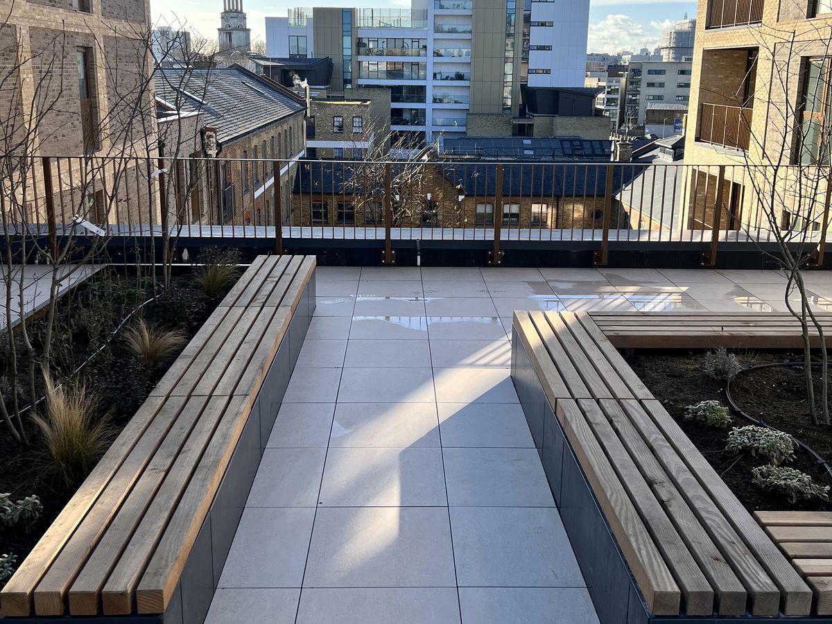 Timber bench seating integrated into metal planters on a porcelain roof terrace