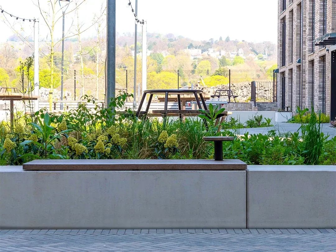 Timber seating and picnic tables among planted beds in a shared courtyard